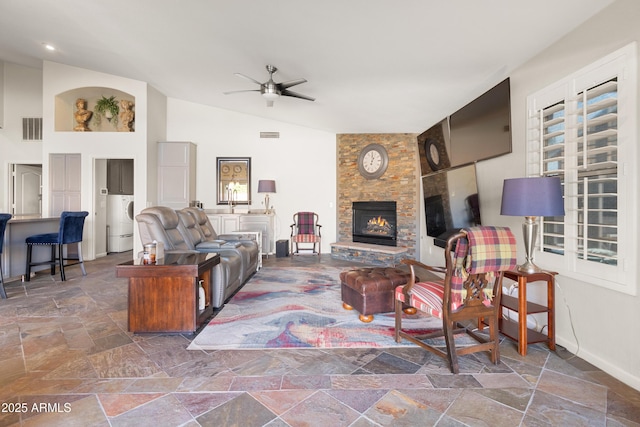 living room featuring washer / dryer, vaulted ceiling, ceiling fan, and a stone fireplace