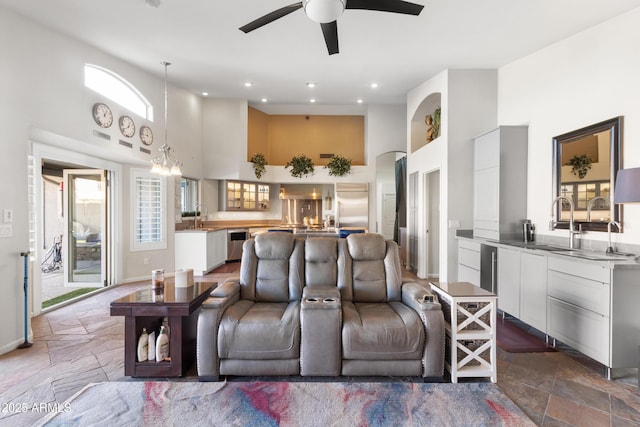 living room featuring sink, ceiling fan with notable chandelier, and a high ceiling