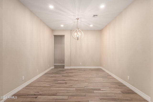 spare room with a notable chandelier and light hardwood / wood-style floors