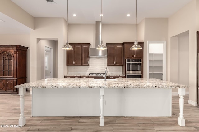 kitchen featuring decorative backsplash, a large island with sink, wall chimney exhaust hood, and a breakfast bar area