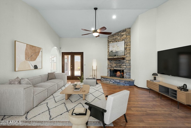 living room with high vaulted ceiling, wood finished floors, french doors, arched walkways, and a stone fireplace