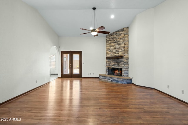 unfurnished living room featuring a fireplace, french doors, wood finished floors, arched walkways, and high vaulted ceiling