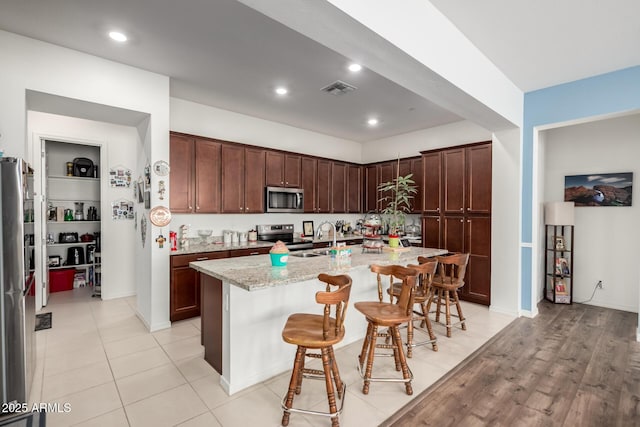 4044 E Dawson Dr E, Chandler, AZ 85249 - kitchen with stainless steel appliances, a kitchen breakfast bar, a center island with sink, a sink, and light stone counters