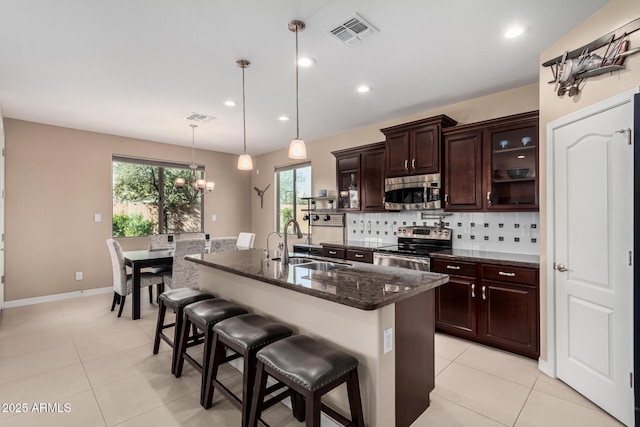 kitchen featuring tasteful backsplash, visible vents, appliances with stainless steel finishes, a kitchen breakfast bar, and a sink