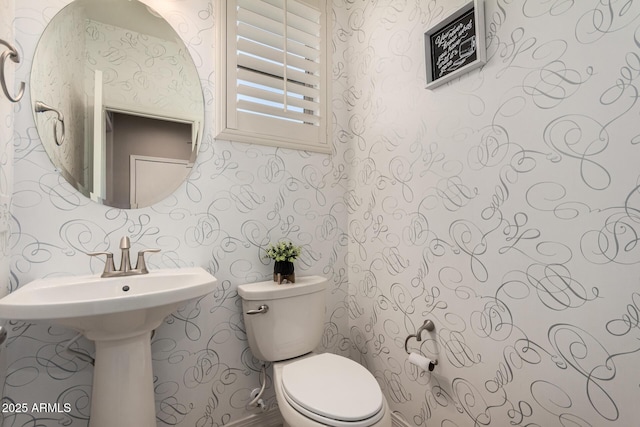 bathroom featuring a sink, toilet, and wallpapered walls