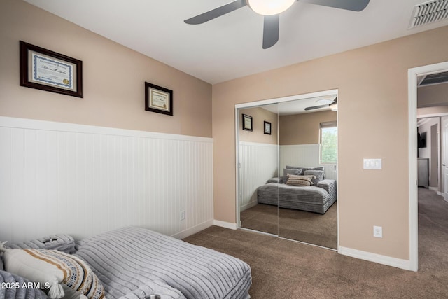 carpeted bedroom with ceiling fan, visible vents, a closet, and wainscoting