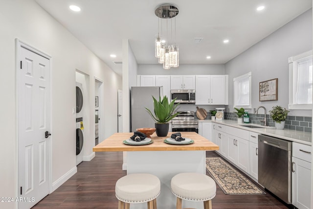 kitchen with a center island, stacked washer and clothes dryer, sink, appliances with stainless steel finishes, and white cabinetry