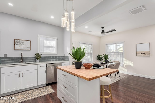 kitchen with butcher block counters, sink, hanging light fixtures, stainless steel dishwasher, and white cabinets