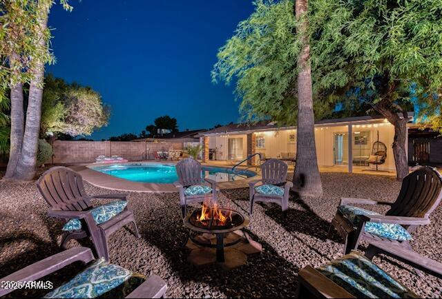 pool at night featuring a patio and a fire pit