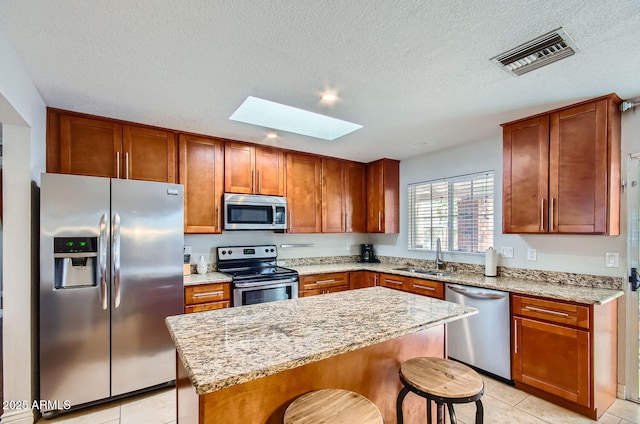 kitchen featuring a breakfast bar, sink, a skylight, appliances with stainless steel finishes, and a kitchen island