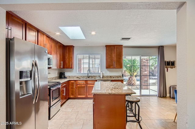 kitchen featuring a kitchen bar, appliances with stainless steel finishes, a skylight, light tile patterned floors, and a center island