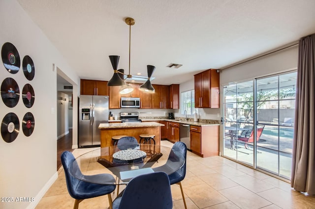 kitchen with a center island, light stone counters, decorative light fixtures, light tile patterned floors, and appliances with stainless steel finishes