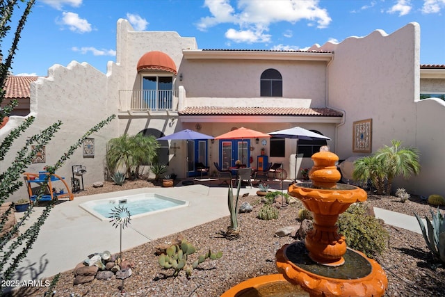 back of property featuring a balcony, stucco siding, a patio area, a jacuzzi, and a tile roof