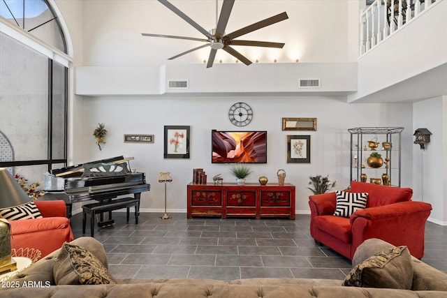 living area featuring a ceiling fan, baseboards, visible vents, and a towering ceiling