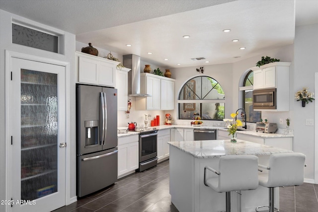 kitchen with wall chimney range hood, white cabinets, stainless steel appliances, and visible vents