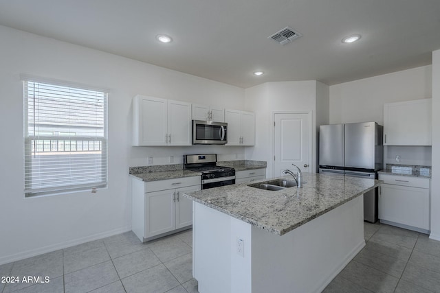 kitchen with light stone counters, stainless steel appliances, sink, white cabinetry, and an island with sink