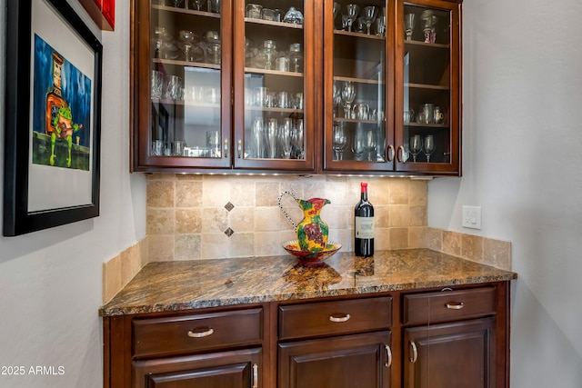 bar featuring backsplash, dark stone counters, and dark brown cabinets