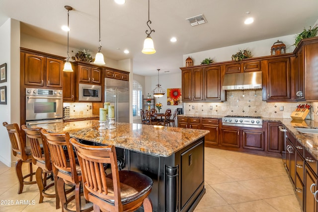 kitchen with a center island, built in appliances, hanging light fixtures, a breakfast bar, and light tile patterned floors