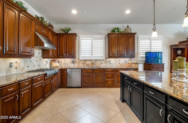 kitchen featuring stainless steel appliances, decorative light fixtures, light stone countertops, range hood, and sink