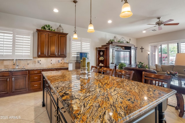 kitchen with ceiling fan, a center island, light tile patterned flooring, dark stone countertops, and sink