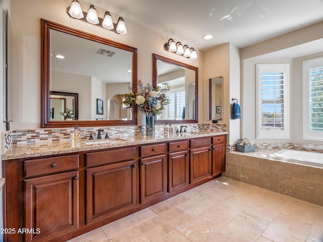 bathroom featuring tasteful backsplash, tiled tub, and vanity