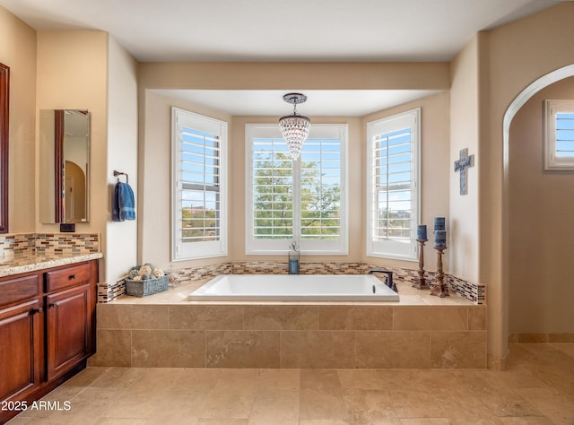 bathroom with vanity, a relaxing tiled tub, and a chandelier