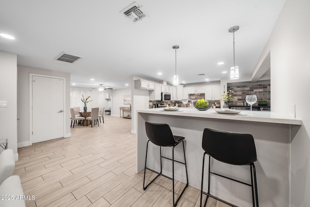 kitchen with tasteful backsplash, visible vents, a peninsula, and stainless steel microwave