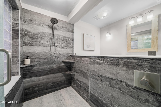 full bathroom featuring a tile shower, visible vents, wainscoting, and tile walls