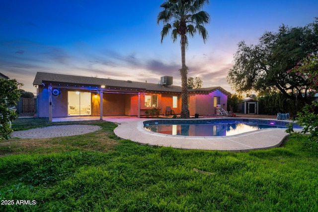 pool at dusk with a storage unit, a yard, an outdoor pool, and a patio area