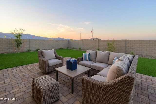 patio terrace at dusk featuring a mountain view, an outdoor hangout area, and a lawn