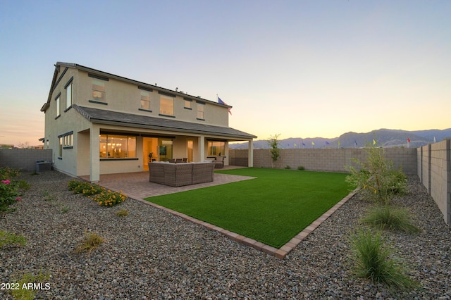 back house at dusk with central AC unit, a yard, outdoor lounge area, a mountain view, and a patio