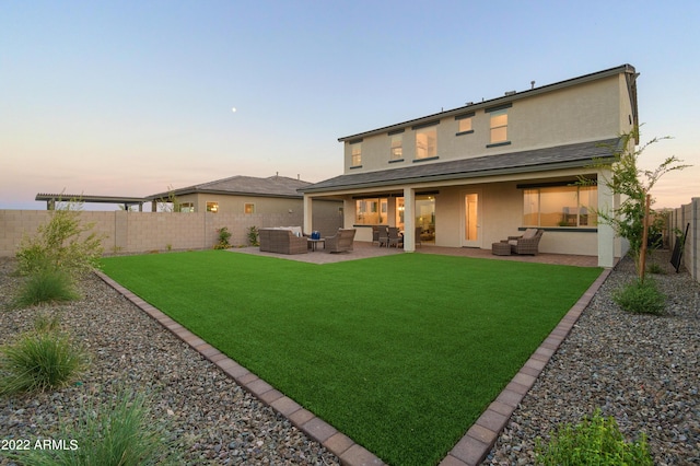 back house at dusk featuring a patio, outdoor lounge area, and a lawn