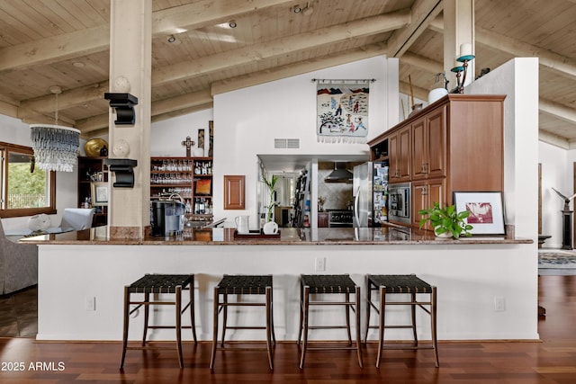 kitchen featuring stainless steel appliances, dark hardwood / wood-style flooring, kitchen peninsula, and dark stone countertops