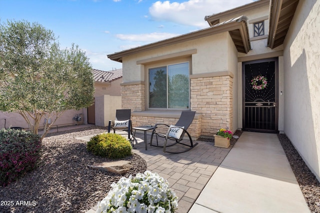 view of exterior entry with stone siding, a patio area, fence, and stucco siding