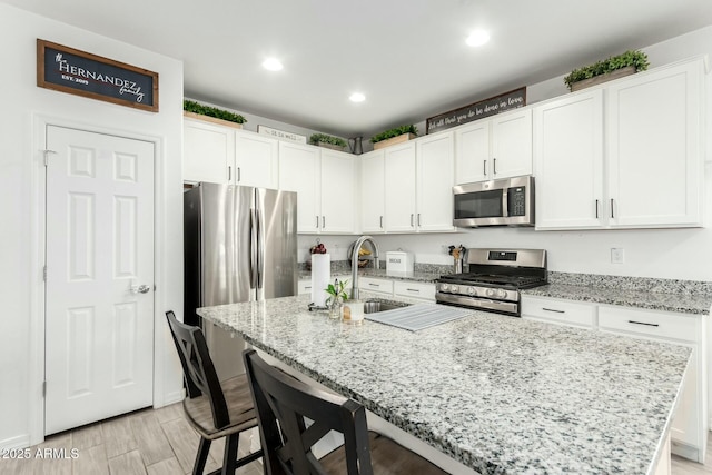 kitchen with light stone countertops, appliances with stainless steel finishes, a breakfast bar area, and white cabinetry