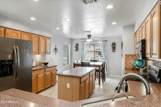 kitchen featuring sink, stainless steel fridge, a kitchen island, ceiling fan, and decorative backsplash