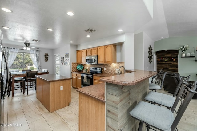 kitchen with a kitchen island, a kitchen bar, decorative backsplash, kitchen peninsula, and stainless steel appliances