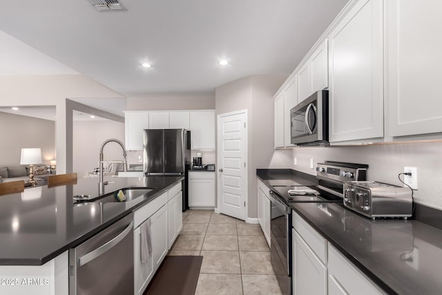 kitchen featuring light tile patterned floors, a sink, appliances with stainless steel finishes, white cabinetry, and dark countertops