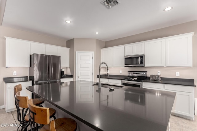 kitchen featuring visible vents, a sink, stainless steel appliances, a kitchen bar, and dark countertops