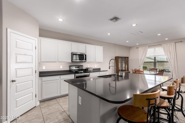 kitchen with visible vents, a center island with sink, a sink, dark countertops, and stainless steel appliances