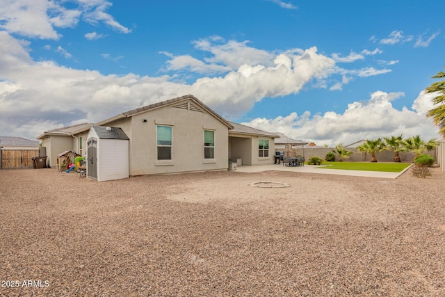 back of house featuring stucco siding, a storage shed, a fenced backyard, an outdoor structure, and a patio