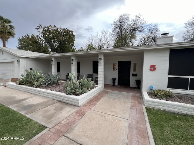 ranch-style house with a garage, a porch, a chimney, and concrete block siding