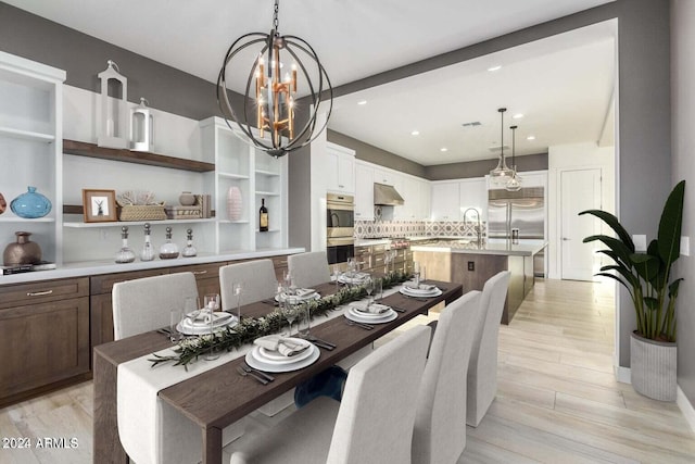 dining area with light wood-type flooring, an inviting chandelier, and sink