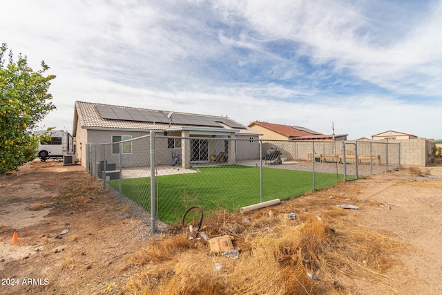 rear view of property featuring a lawn, solar panels, and central air condition unit