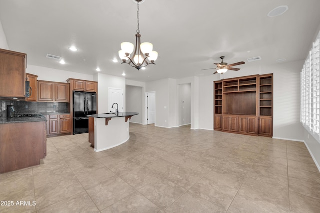kitchen with freestanding refrigerator, dark countertops, a breakfast bar area, and ceiling fan with notable chandelier
