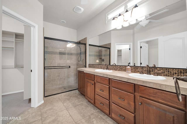 bathroom with backsplash, a sink, a walk in closet, and a stall shower
