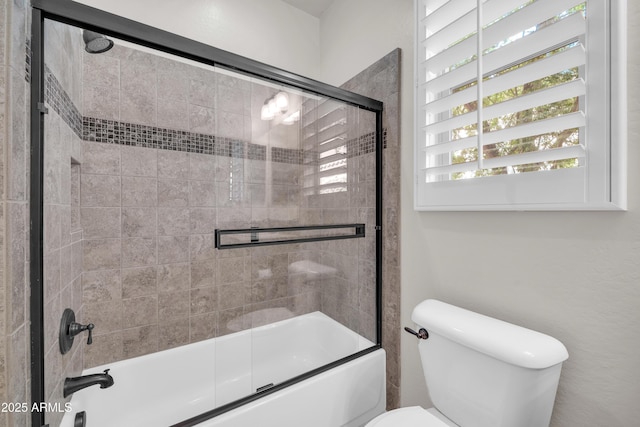bathroom with toilet and shower / bath combination with glass door
