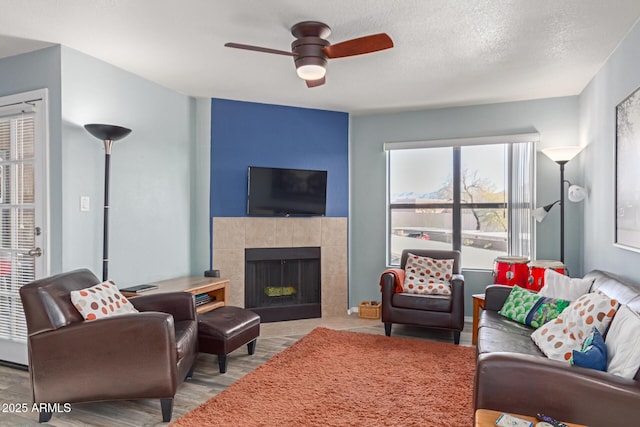 living room with ceiling fan, a tiled fireplace, light hardwood / wood-style floors, and a textured ceiling