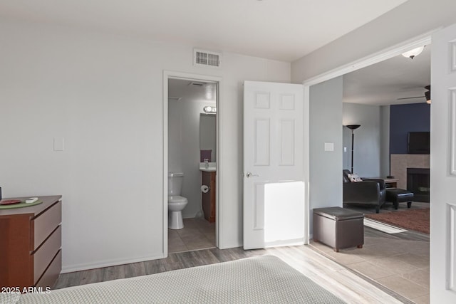 bedroom with light wood-type flooring, a fireplace, and ensuite bath