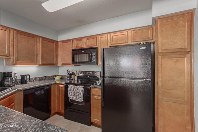 kitchen with light tile patterned floors, dark stone counters, and black appliances